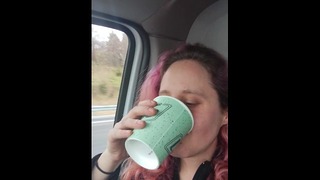 Flickvän dricker en stor kopp mycket gult piss i bilen.
